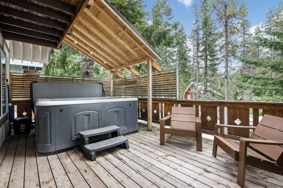 A tranquil exterior scene featuring a private hot tub nestled on a wooden deck, surrounded by tall pine trees. The hot tub is the focal point, inviting guests to relax while immersed in nature. The deck’s design and the trees create a secluded, peaceful ambiance ideal for unwinding after mountain adventures.