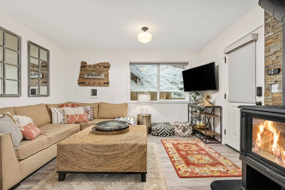 A plush sofa and coffee table are arranged before a glowing fireplace, with a window offering soft natural light. The room exudes warmth and comfort, inviting guests to relax and socialize or simply enjoy the ambiance.