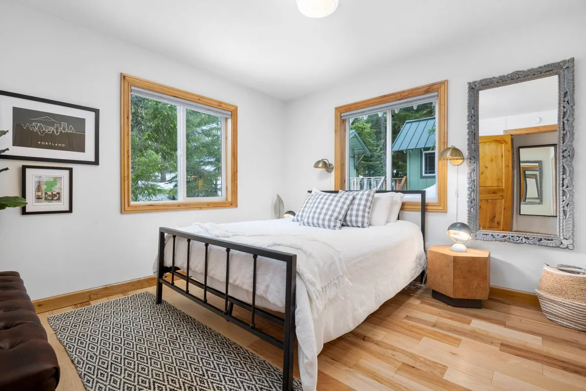 A serene bedroom with a well-made bed adorned with patterned pillows, a large mirror reflecting the natural light streaming through generous windows, and a tranquil atmosphere ideal for relaxation.