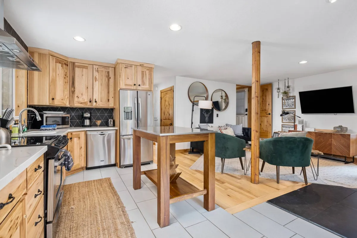 This image captures a warm, inviting kitchen space with a kitchen island, green chairs, wooden cabinetry, and a television in view. The setup suggests a space ideal for cooking, gathering, and entertaining, with cozy yet practical seating around the island.