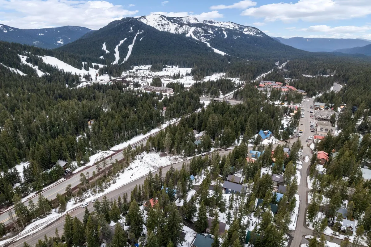 A panoramic view of Mt. Hood’s snow-covered slopes, backed by a majestic mountain range and dense forest, with a small ski town and resort buildings nestled in the valley. Skiers and snowboarders can be seen on the slopes, evoking a sense of adventure and winter excitement.